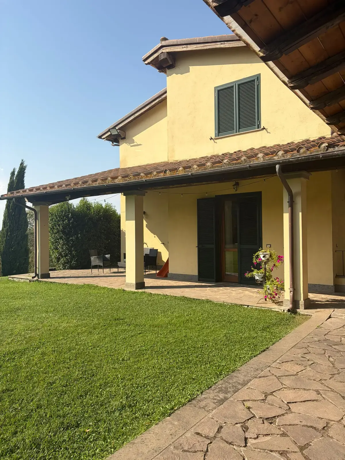 Il fianco della casa con il porticato e il vialetto in pietra che attraversa il prato