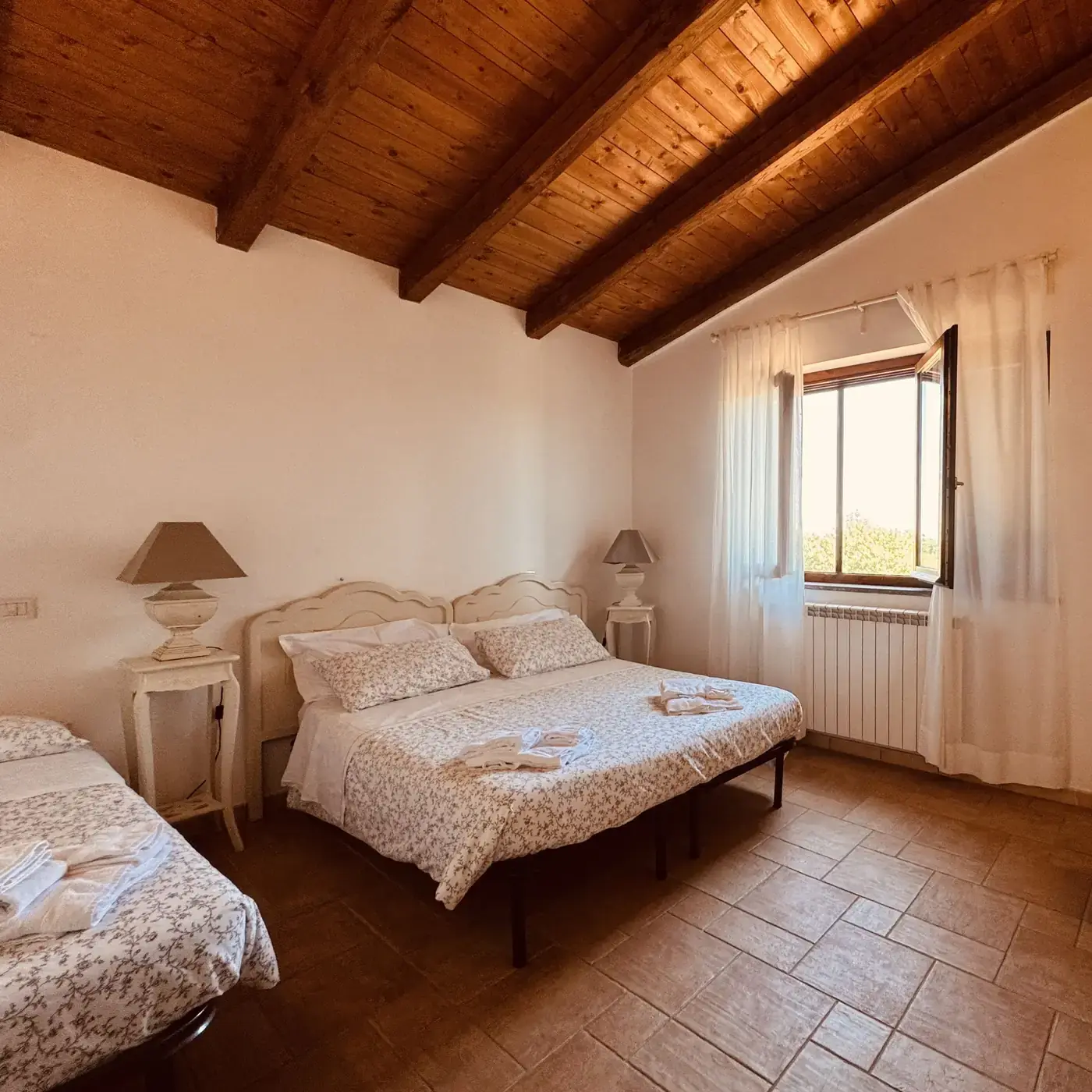 Camera dell'Oasi del Verde con travi in legno a vista, letto matrimoniale e letto singolo, illuminata dalla luce della finestra